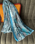 Blue patterned scarf draped over a gray couch with orange cushions.