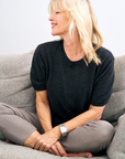 Woman sitting on a gray couch wearing a charcoal cashmere sweater and gray pants.