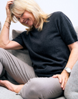 Woman sitting on a couch wearing a charcoal cashmere knit and gray pants, smiling.