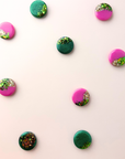 Colorful round scarf magnet brooches with green and pink accents on a light pink background