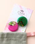 Two colorful brooches on a 'Cara Cashmere' branded card with a beige background.