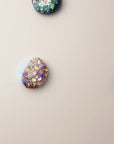 Colorful round scarf magnet brooches with in navy and white with sparkle accents on a light pink background