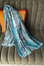 Blue patterned scarf draped over a gray couch with orange cushions.