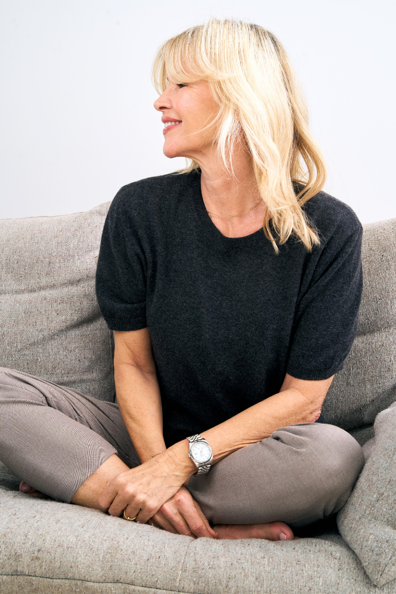 Woman sitting on a gray couch wearing a charcoal cashmere sweater and gray pants.