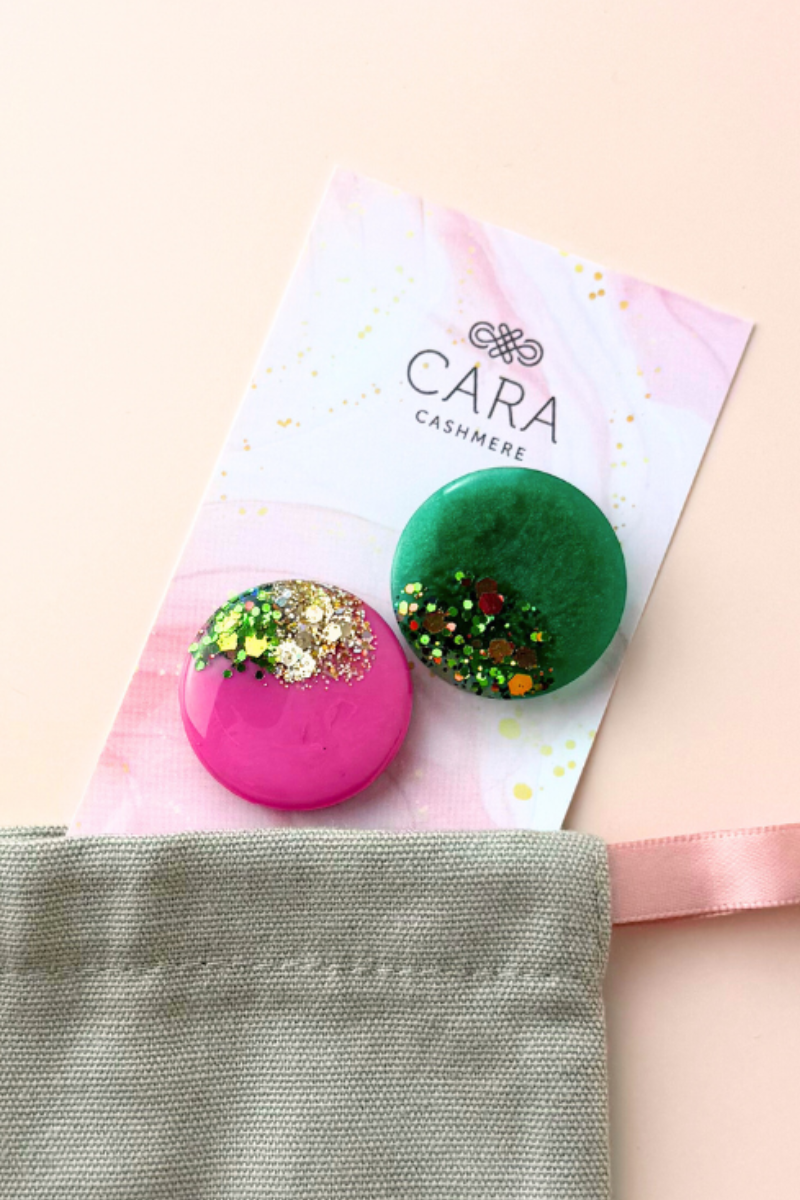 Two colorful brooches on a 'Cara Cashmere' branded card with a beige background.