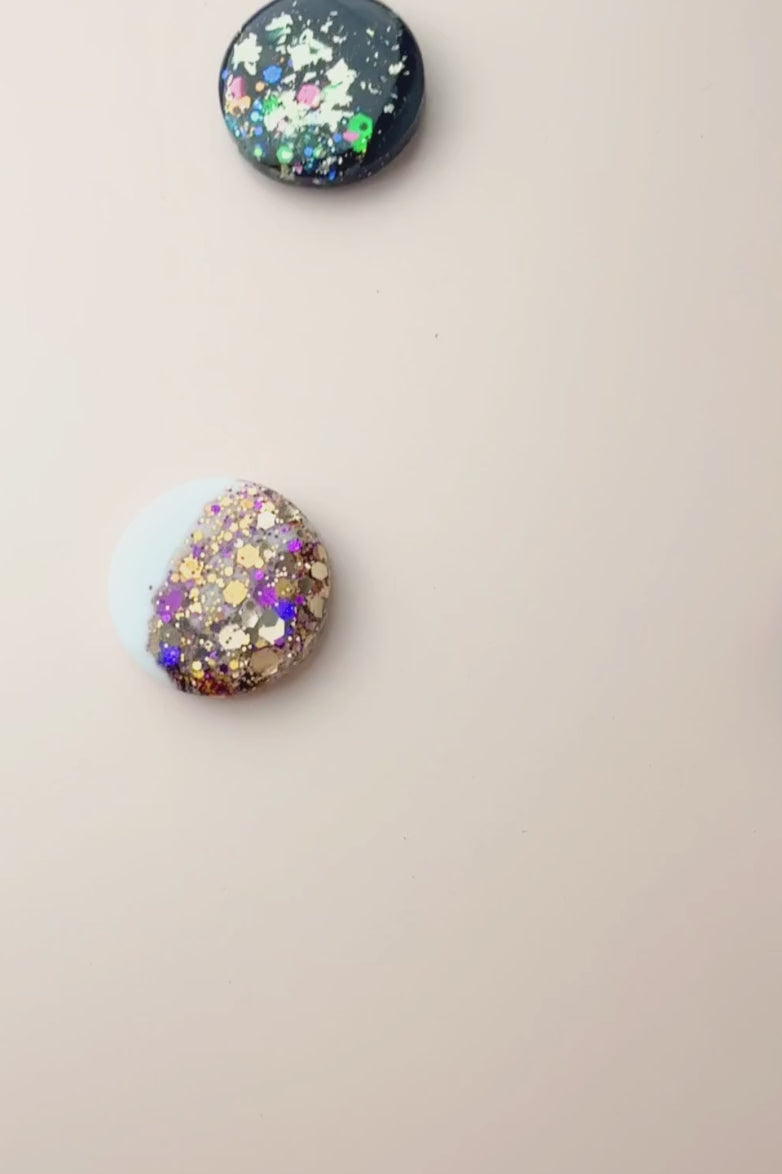 Colorful round scarf magnet brooches with in navy and white with sparkle accents on a light pink background